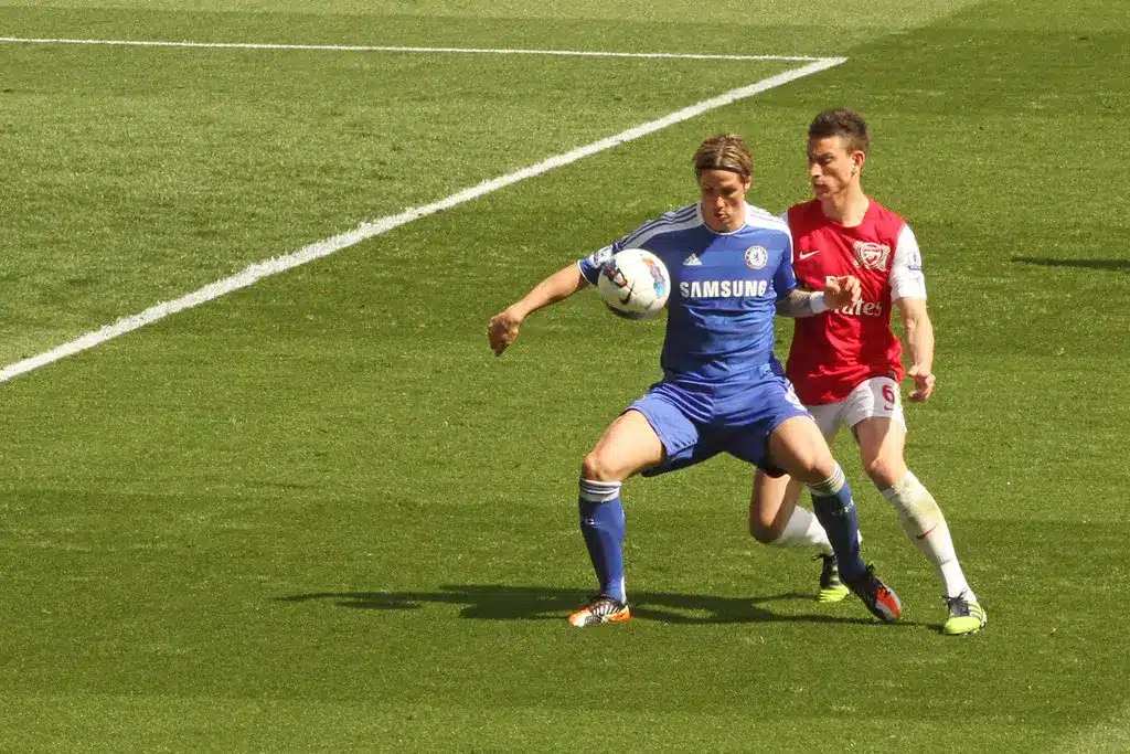 Ο Fernando Torres με μπλε εμφάνιση της Chelsea ελέγχει την μπάλα με τον Laurent Koscielny πίσω του.